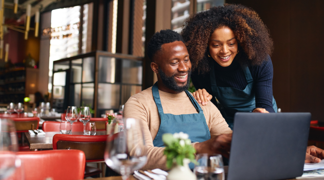 Un homme et une femme propriétaires d'entreprise sont assis dans la salle à manger de leur restaurant et regardent les outils numériques #JeChoisisPME destinés aux propriétaires d'entreprise.
