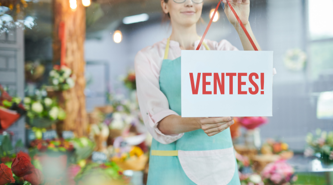 Une femme propriétaire d'une PME accroche une pancarte « ventes! » dans la vitrine de son magasin de fleurs.