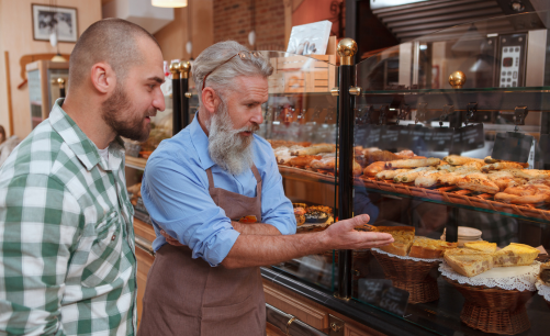 l'heureux propriétaire d'une boulangerie locale montrant à un client un assortiment de produits de boulangerie dans une vitrine comprenant des quiches, des scones et des pâtisseries