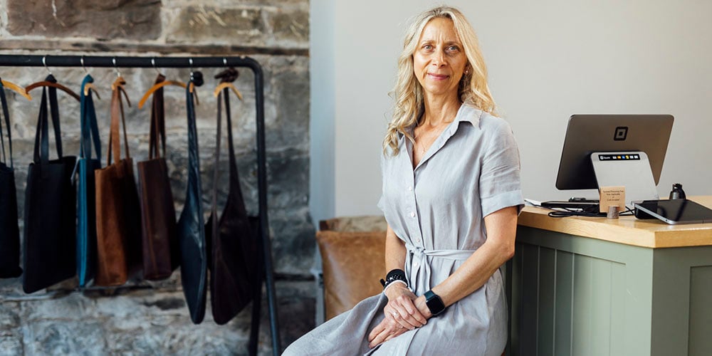 Tabitha proudly sits in her store beside a selection of her handmade leather bags